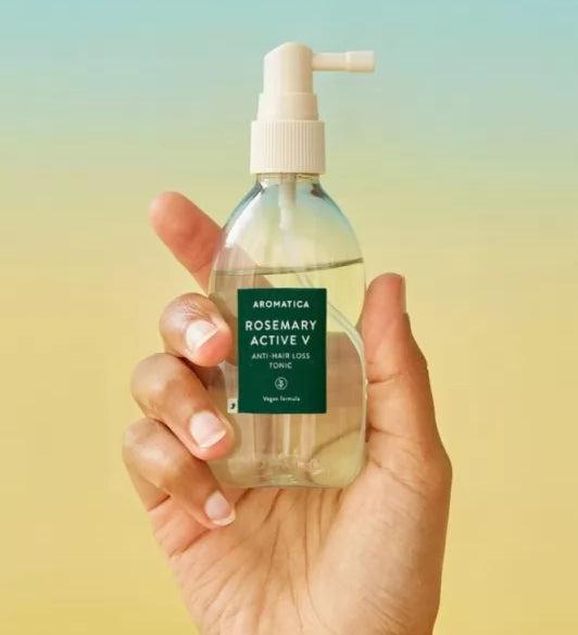 Прозора пляшечка з білим дозатором засобу Aromatica Rosemary Active V Anti-Hair Loss Tonic у руці на жовтому-блакитному фоні, 100 мл