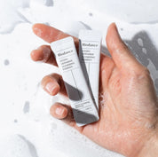 У долоні лежать два саше, рука трохи опущена у воду, і вся у піні.