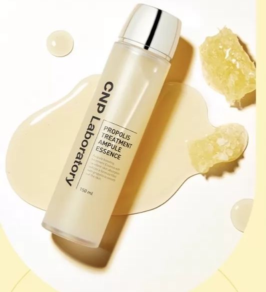 Напівпрозора пляшка з жовтою есенцією та сріблястою кришечкою, CNP Laboratory Propolis Treatment Ampoule Essence, лежить в жовтій рідині поряд із частиною медових сот.