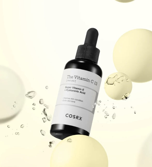 Чорна пляшечка з білою етикеткою та чорною піпеткою сироватки COSRX The Vitamin C 23 Serum зависла у повітрі на жовтій кульці.