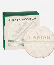 Твердий шампунь LABO-H у зручній круглій формі бежевого кольору з темними вкрапленнями, на фоні упаковка