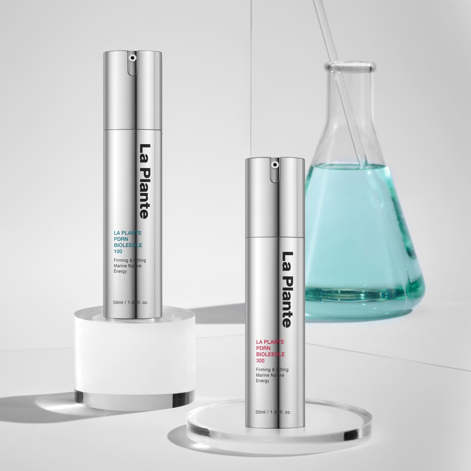 Набір PDRN Bioleedle 300 і PDRN Bioleedle 100 — дві сироватки у сірих пляшечках стоять на скляних подіумах, на фоні видно хімічну колбу з блакитною рідиною всередині.