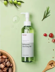 На зеленій поверхні лежить пляшечка засобу Ma:nyo Herb Cleansing Oil, поряд — різні ягоди та рослинність.
