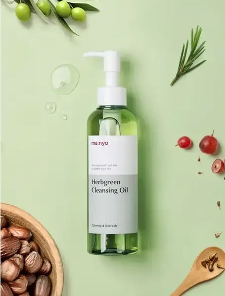 На зеленій поверхні лежить пляшечка засобу Ma:nyo Herb Cleansing Oil, поряд — різні ягоди та рослинність.