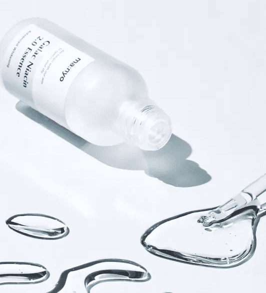 Відкрита пляшечка есенції Ma:nyo Niacin Essence лежить на білій поверхні, поруч — розлита есенція та піпетка.