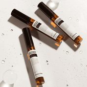 Три ампули сироватки NARD Long And Glam Intensive Eyelash Serum лежать на білій поверхні, вкритій крапельками води.