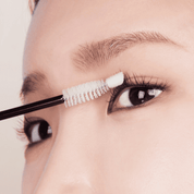 Дівчина наносить сироватку NARD Long And Glam Intensive Eyelash Serum білою щіточкою на вії.