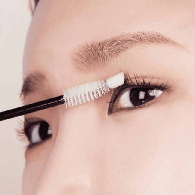 Дівчина наносить сироватку NARD Long And Glam Intensive Eyelash Serum білою щіточкою на вії.