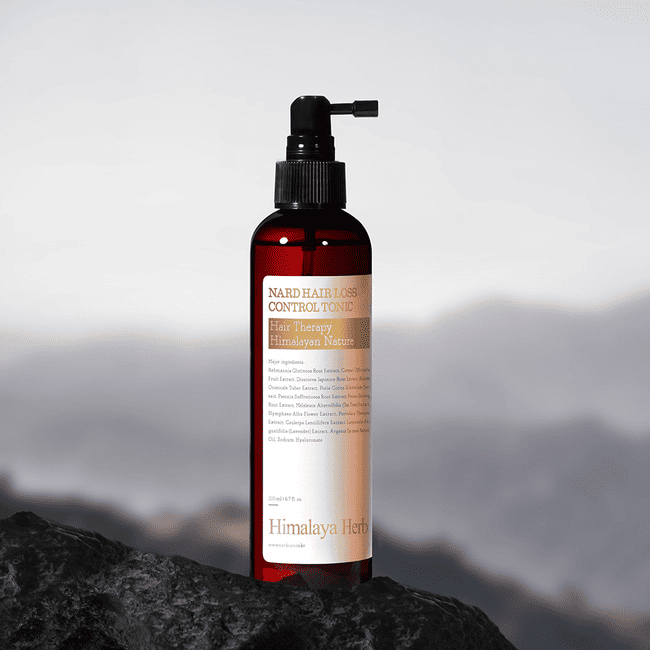 Прозора коричнева пляшечка з чорним дозатором засобу NARD Hair Loss Control Tonic стоїть на камені.