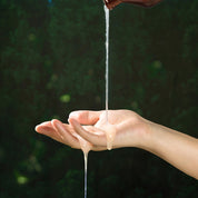 Світла гелева текстура шампуню, яка стікає з пляшки на відкриту долоню на фоні зеленого листя