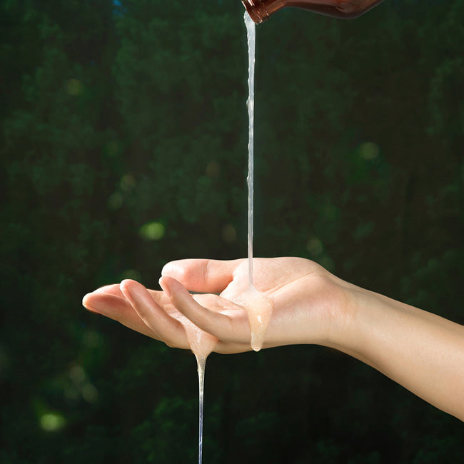 Світла гелева текстура шампуню, яка стікає з пляшки на відкриту долоню на фоні зеленого листя