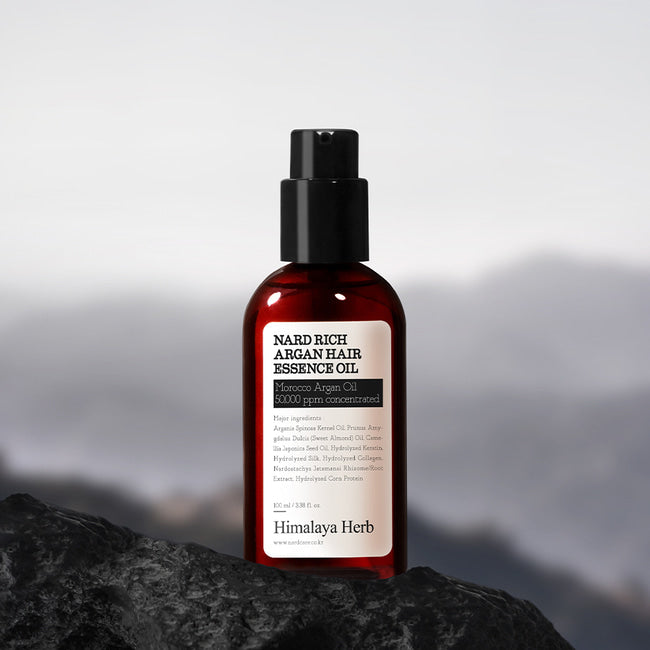 Темно-прозорий флакон з чорним дозатором олії-есенції для волосся Nard Rich Argan Hair Essence Oil стоїть на білому фоні.