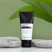 Темно-коричневий тюбик засобу Nard Intensive Hair Pack стоїть на поверхні біля сірих каменів на фоні зеленого листя