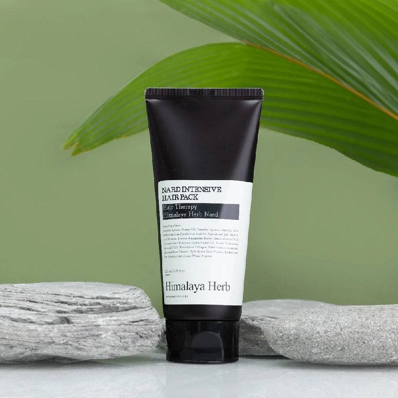 Темно-коричневий тюбик засобу Nard Intensive Hair Pack стоїть на поверхні біля сірих каменів на фоні зеленого листя