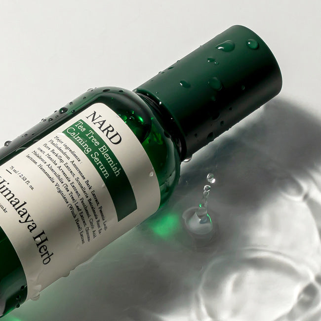 Ампула сироватки Bouquet Garni Nard Tea Tree Blemish Calming Serum лежить на білій поверхні, покритій прозорою водою.