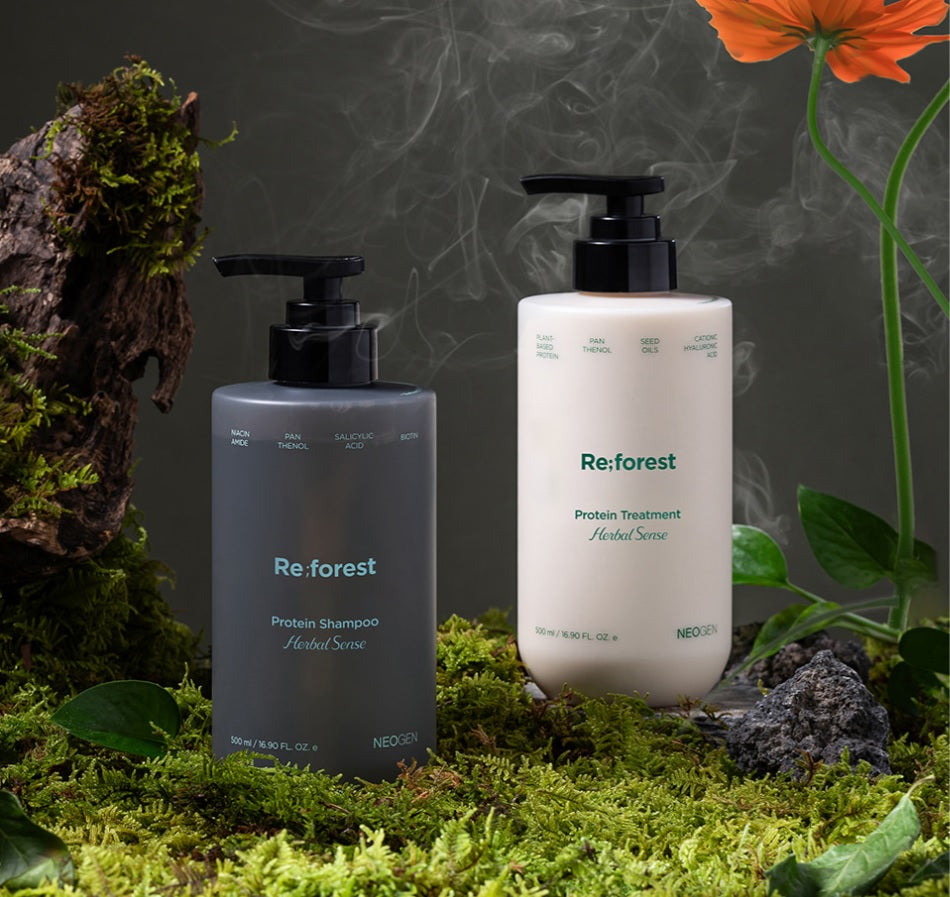 Сірий шампунь та білий кондиціонер Neogen Re;forest з чорними дозаторами на траві серед каменів з оранжевими квітками та легким димом.