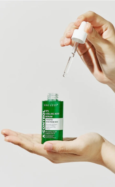 Людина тримає в одній руці ампулу сироватки Nine Less A-Control 10% Azelaic Acid Serum, а іншою рукою дістає з неї піпетку.