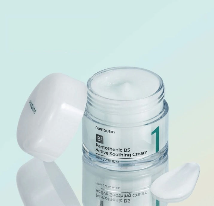 Відкрита скляна баночка з білою кришкою крему Numbuzin No.1 Pantothenic B5 Active Soothing Cream стоїть біля розмазаної текстури крему, кришка оперта на баночку.
