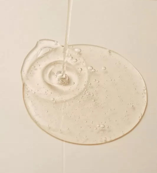 Текстура сироватки ROUND LAB Mugwort Calming Serum розливається на світлу поверхню, утворюючи тонкий шар.