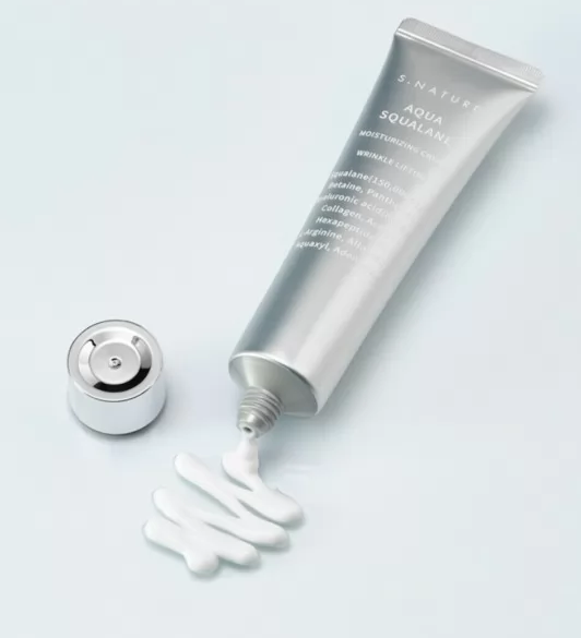 Відкритий тюбик крему SNature Aqua Squalane Moisturizing Cream лежить на поверхні, з нього ніжно витікає крем, створюючи плавний слід