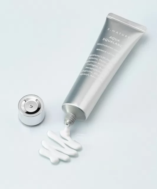 Відкритий тюбик крему SNature Aqua Squalane Moisturizing Cream лежить на поверхні, з нього ніжно витікає крем, створюючи плавний слід