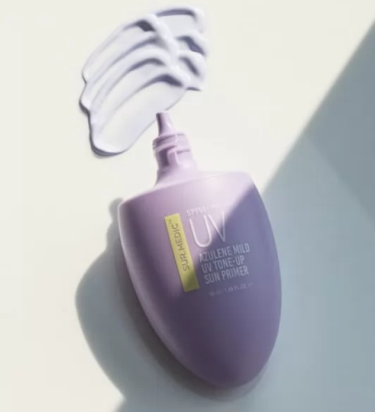 На фото відкритий тюбик Azulene Mild Tone-up Cream, біля нього текстура крему нанесена на білу поверхню.