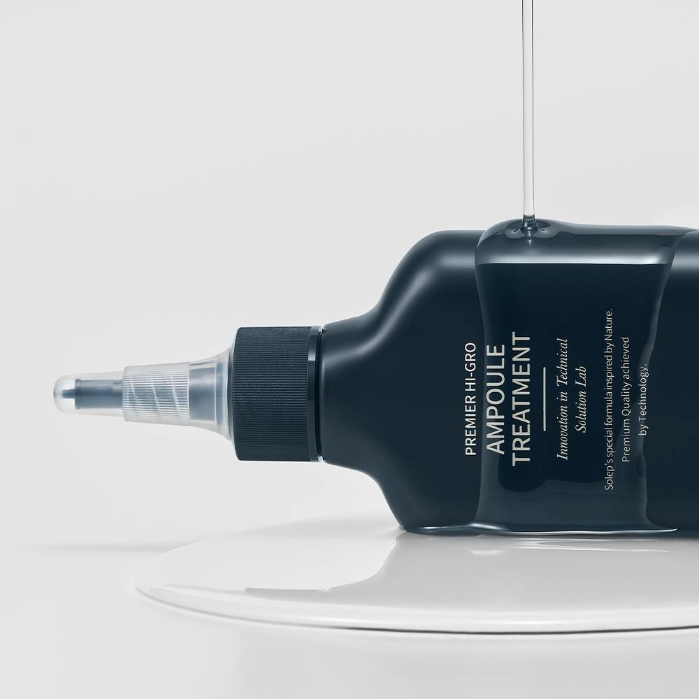 Синя пляшечка засобу Solep Premier Hi-gro Ampoule Treatment лежить на білій поверхні, а на неї виливається текстура цієї есенції.