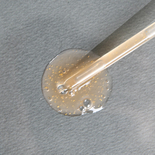 На сірій поверхні з піпетки налита текстура засобу Sur.Medic+ 24k Gold Repair Ampoule.