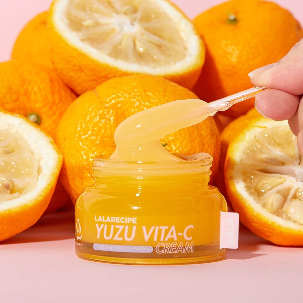 Вітамінний крем для обличчя LALARECIPE Yuzu Vita C Cream на шпателі з екстрактом юдзу на фоні свіжих плодів