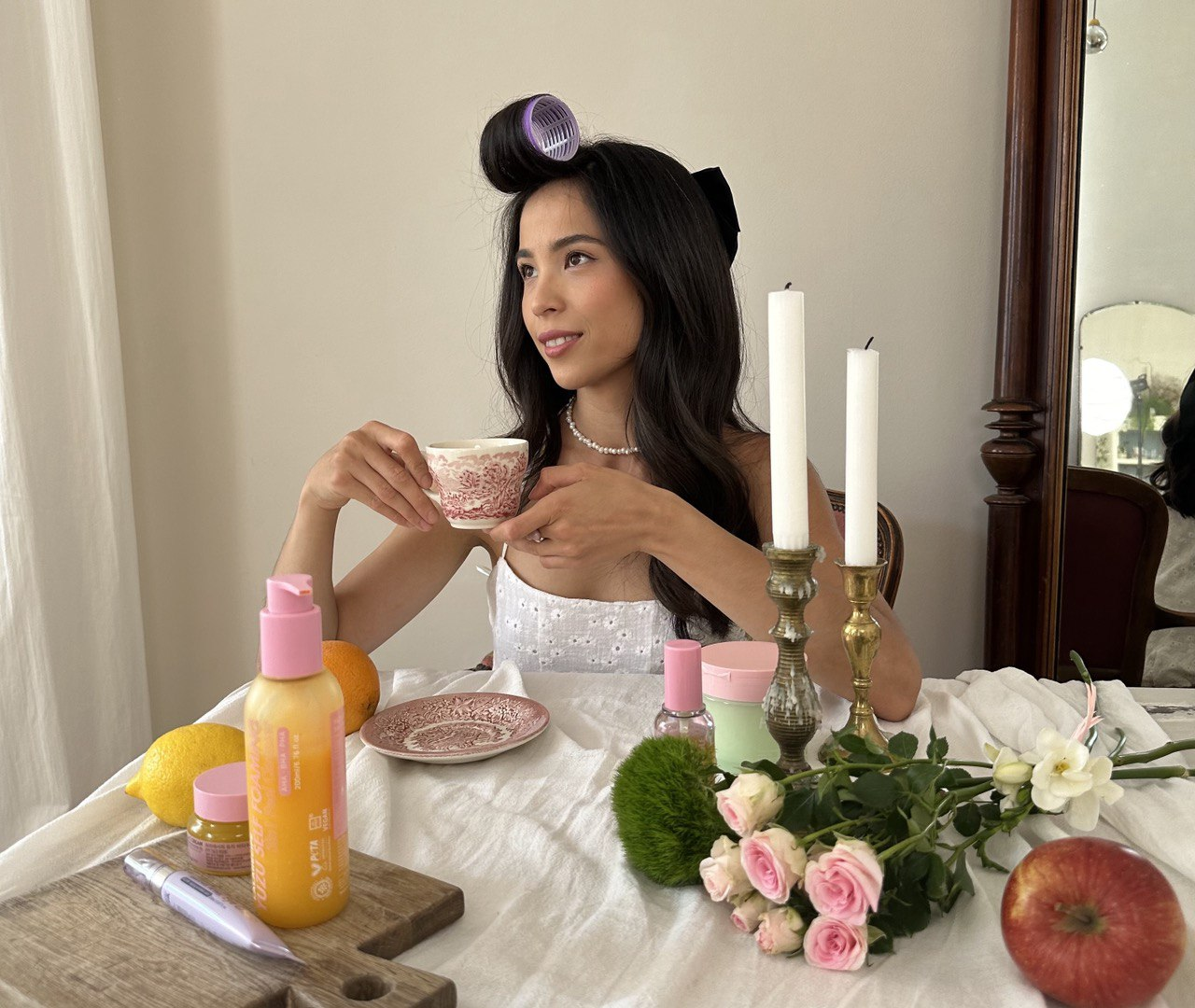 Жінка з чашкою чаю за столом, поруч LALARECIPE Yuzu Self Foaming 3in1 Cleanser і цитрусові.