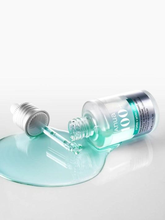 На білий поверхні лежить відкритий флакон засобу ANUA PDRN Hyaluronic Acid Capsule 100 Serum, з якого витікає бірюзова сироватка, піпетка лежить поряд.