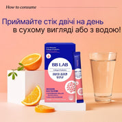 Синьо-рожева коробка та саше колагену BB LAB Low-Molecular Collagen Probiotics стоять на білому подіумі, поряд розташовані шматочки апельсина і склянка з водою на рожевому фоні.