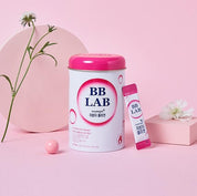 Біло-рожева баночка BB Lab Good Night Collagen поряд із саше, на маленькому подіумі з квіткою, а також поруч кулька на фоні квітки.