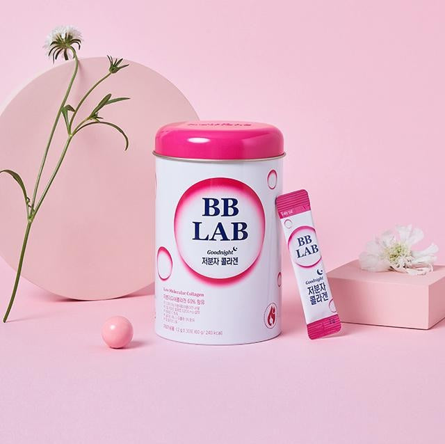 Біло-рожева баночка BB Lab Good Night Collagen поряд із саше, на маленькому подіумі з квіткою, а також поруч кулька на фоні квітки.