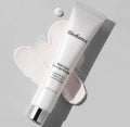 Білий тюбик Biodance Skin Glow Tone Up Booster 30 мл з чорними написами та сріблястою кришечкою лежить на кремовій текстурі, нанесеній на білу поверхню