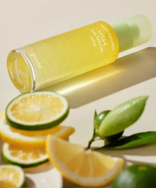 Пляшечка Goodal Green Tangerine Vita C Dark Spot Care Serum лежить на білій поверхні, поруч з нею видно шматочки лимону та лайму.