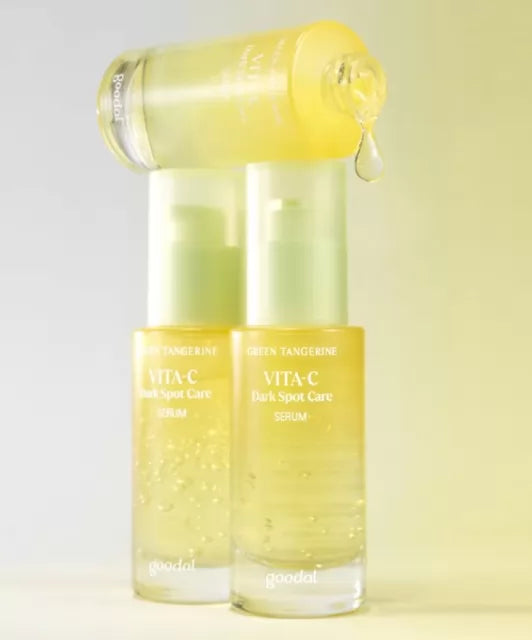 Стоять дві закриті пляшечки Goodal Green Tangerine Vita C Dark Spot Care Serum на них лежить відкрита пляшечка, з якої капає жовтувата есенція.