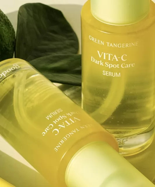 Пляшка Goodal Green Tangerine Vita C Dark Spot Care Serum стоїть, а поряд лежить ще одна пляшка, на фоні видно зелене листя.
