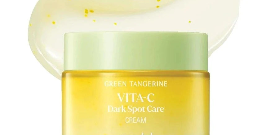 Скляна баночка крему Goodal Green Tangerine Vita C Dark Spot Care Cream з білою кришкою стоїть на білому фоні, на фоні розмазана кремова текстура крему, біло-жовтого кольору з жовтим вкрапленням.