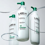 Три флакони шампуню LABO-H із зеленими дозаторами стоять на прозорій скляній поверхні