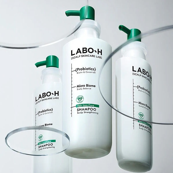 Три флакони шампуню LABO-H із зеленими дозаторами стоять на прозорій скляній поверхні