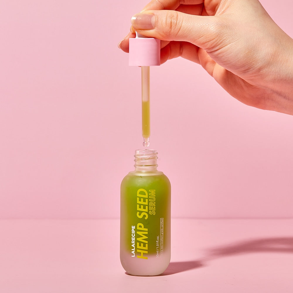 Піпетка з сироваткою LALARECIPE Hemp Seed Serum, що капає в пляшечку на рожевому фоні