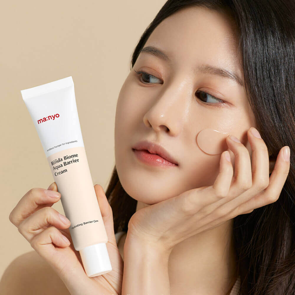 Дівчина ніжно тримає крем Ma:nyo Bifida Biome Aqua Barrier Cream в одній руці, іншою обережно наносить засіб під око 