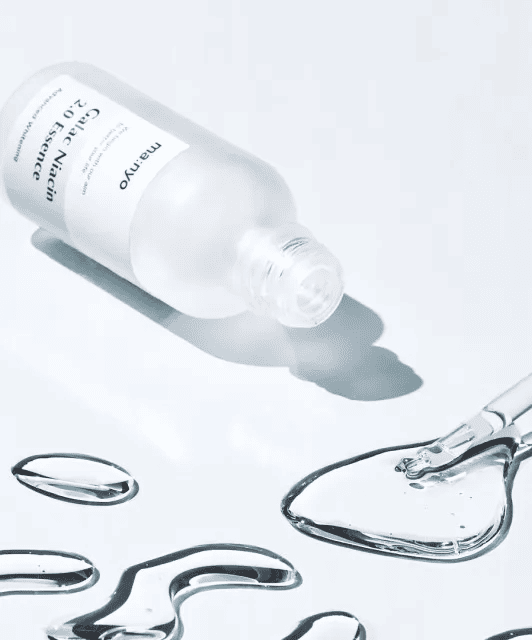 Відкрита пляшечка есенції Ma:nyo Niacin Essence лежить на білій поверхні, поруч — розлита есенція та піпетка.