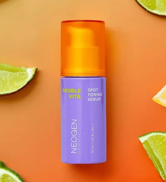Фіолетова баночка з оранжевою кришечкою Neogen Dermalogy Double Vita Spot Toning Serum лежить на оранжевій поверхні поряд із порізаними лаймами.