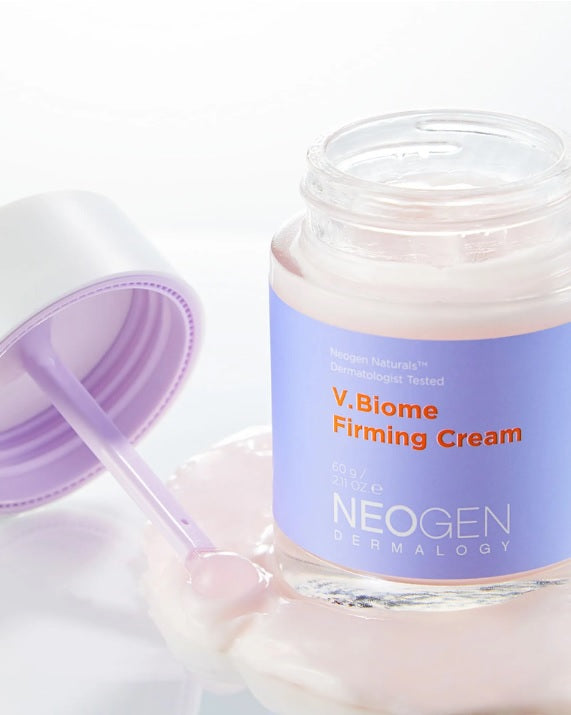 Баночка крему Neogen Dermalogy V.Biome Firming Cream стоїть на поверхні, покритій ніжним шаром крему, поруч лежить кришечка.