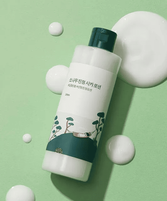 Альт текст: Світло-зелена баночка лосьйону ROUND LAB Pine Calming Cica Lotion лежить на зеленій поверхні, поруч розлита, білими плямами, текстура лосьйону