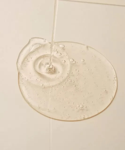 Текстура сироватки ROUND LAB Mugwort Calming Serum розливається на світлу поверхню, утворюючи тонкий шар.