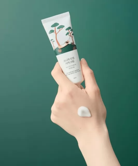 Тюбик крему Round Lab Pine Calming Cica Cream в руці, на шкірі руки видно нанесений крем.