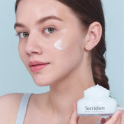 Дівчина тримає відкриту баночку крему Torriden Dive-In Soothing Cream біля шиї, крем нанесений під її оком.